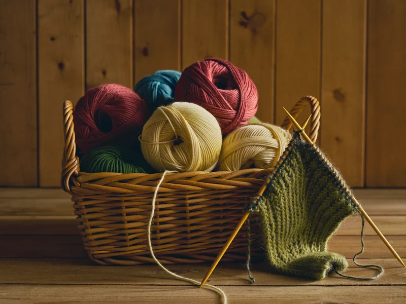 Illustrierte Wollknäuel im Korb neben Holznadeln und einem Strickstück